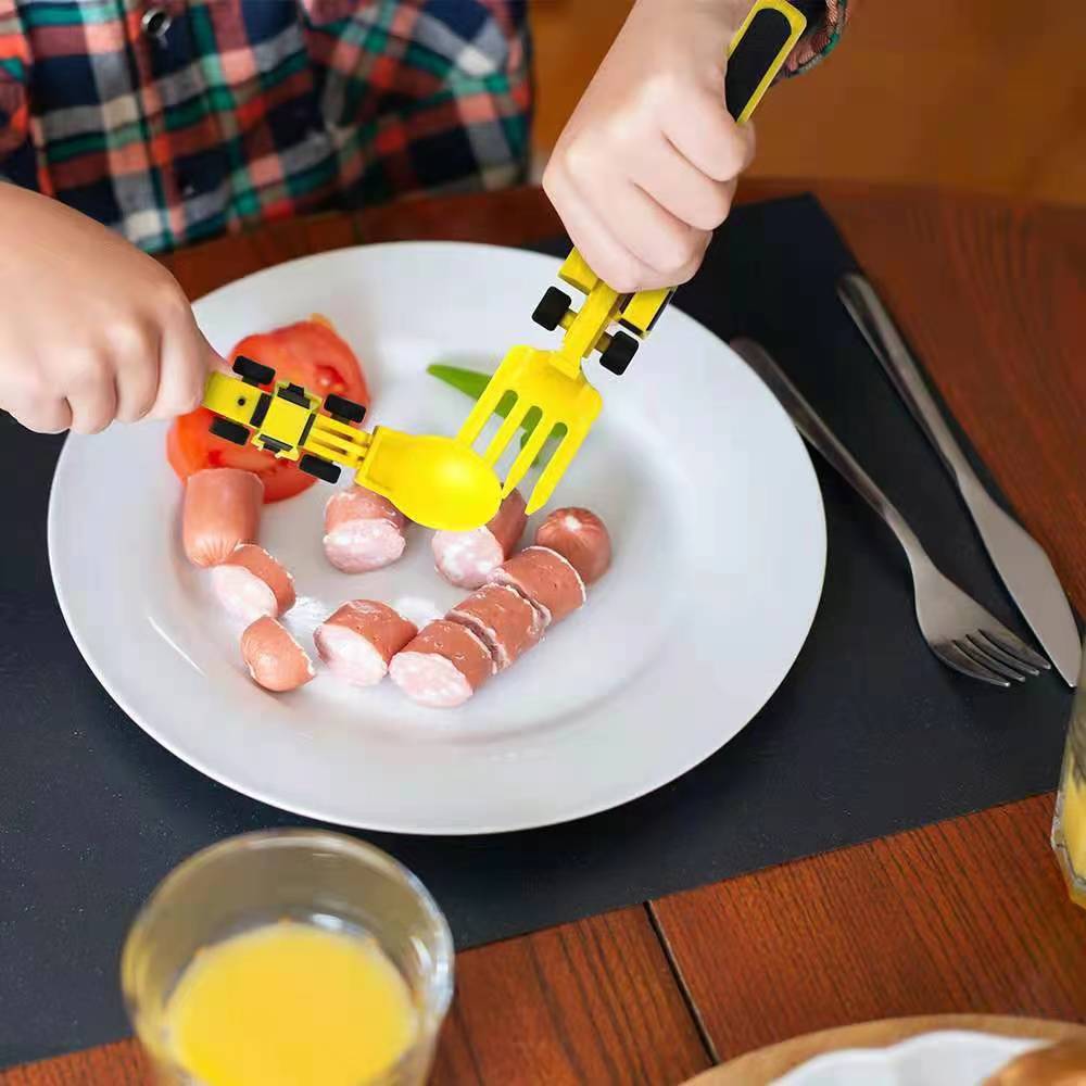 Plato blanco con salchichas y manos usando cubiertos amarillos infantiles de tipo excavadora/carro.