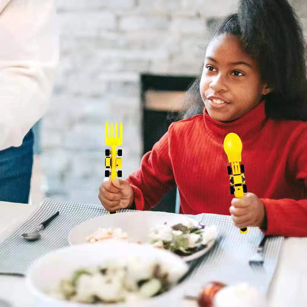 Niña con cubiertos amarillos infantiles en la mano, con plato servido sobre la mesa.