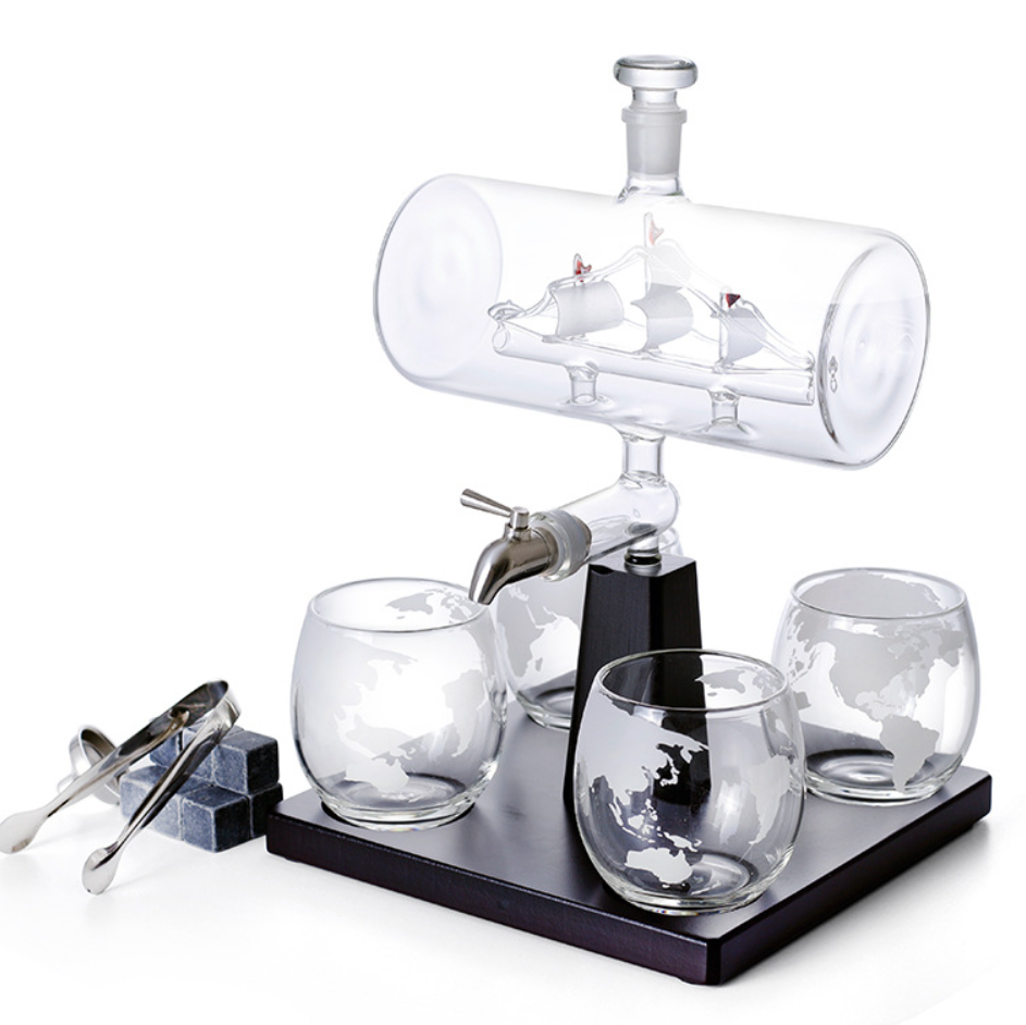 Clear bottle-style wine dispenser on black base with globe-pattern tumblers and tap