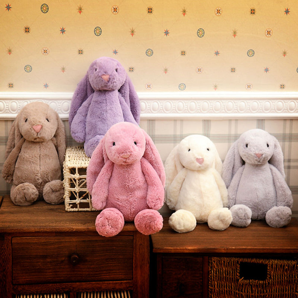 Assorted long-eared bunny plush toys on a wooden bench, pastel colors