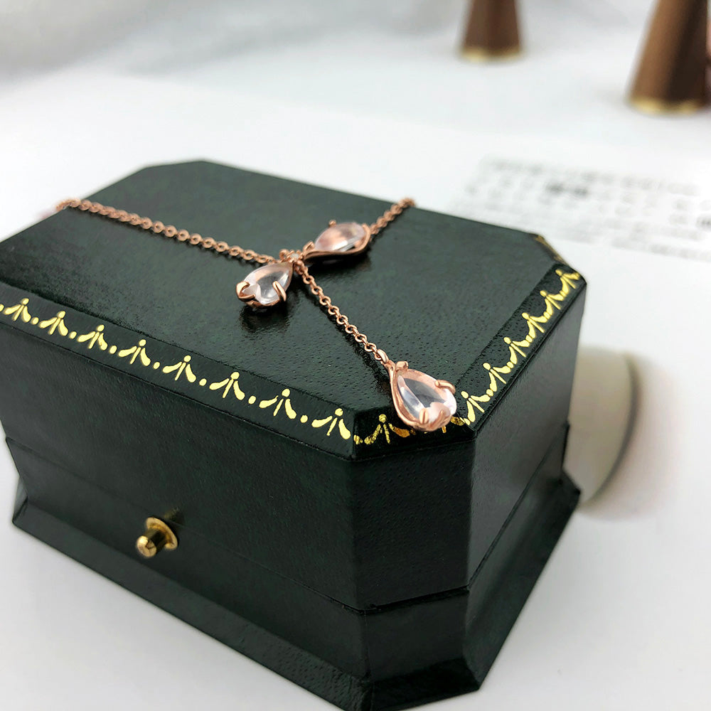 Pink teardrop quartz charms on rose-gold necklace resting on dark jewelry box
