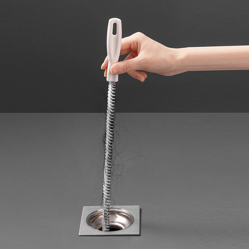 Hand holding white hair-cleaner brush with coiled bristles positioned over a drain
