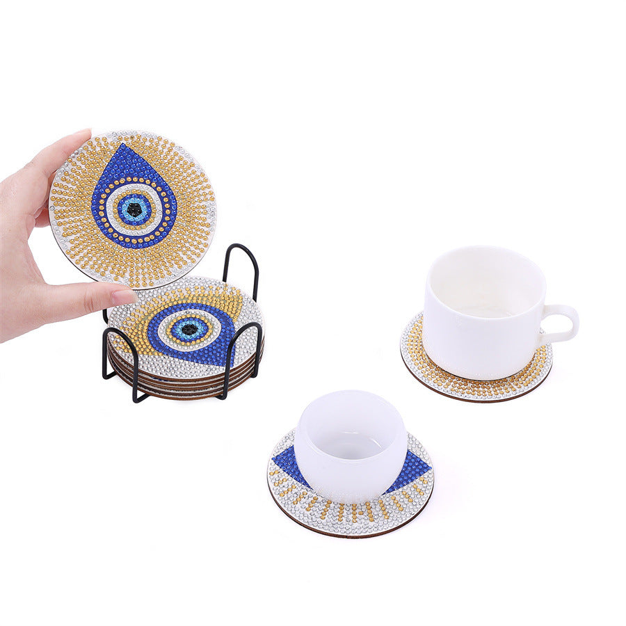 Hand holding round diamond coaster with blue eye motif; mugs on matching coasters