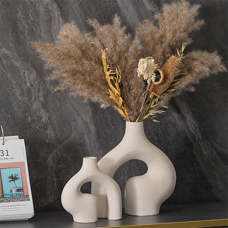 Pair of beige ceramic sculptural vases with curved cut-outs, holding dried stems