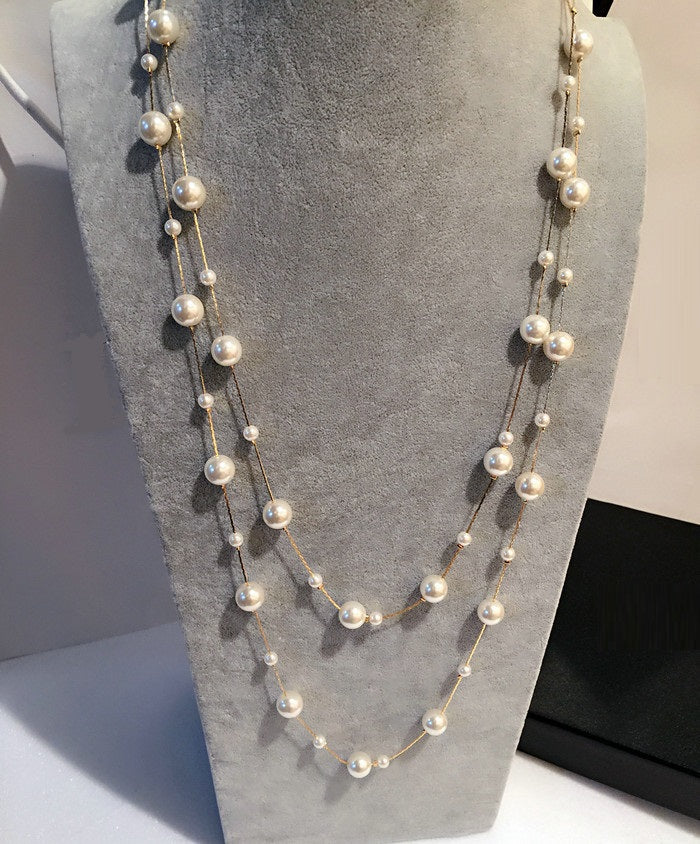 Pearl-like bead chain necklace draped on gray bust, long layered strands