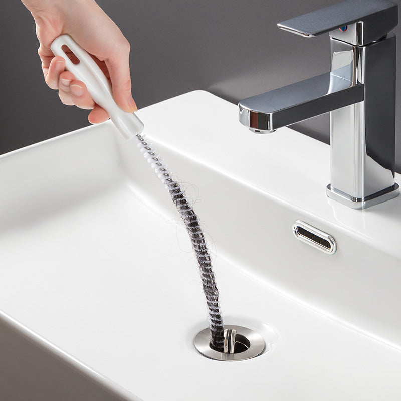 White hair-cleaner brush reaching a sink drain, with long coiled metal bristles