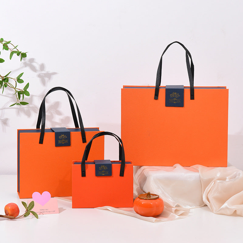 Orange gift box set with black handle straps and logo badge, medium box centered with small box and large lid