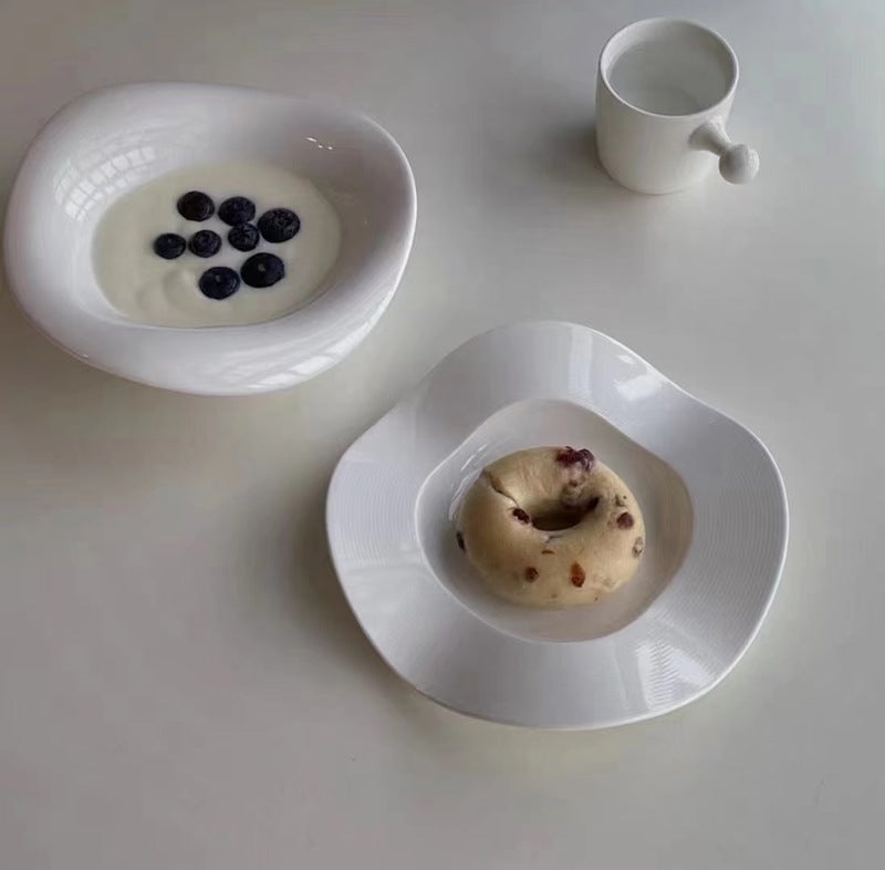 White wave-shaped ceramic snack plates with oval wells, one plate holding a small dessert