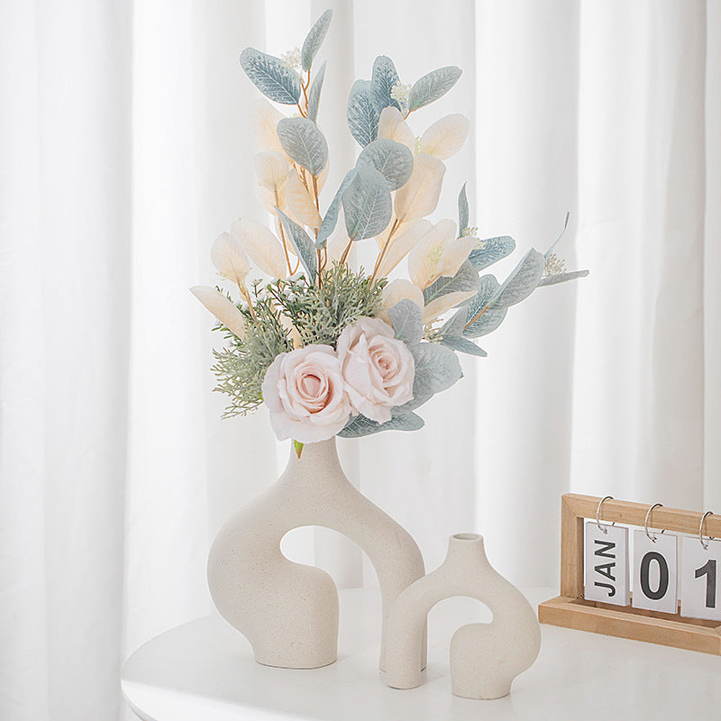 Beige ceramic vase with oval cut-out, holding a bouquet of roses and eucalyptus